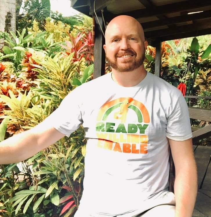 man with ready willing enable shirt smiling at the camera in tropical setting